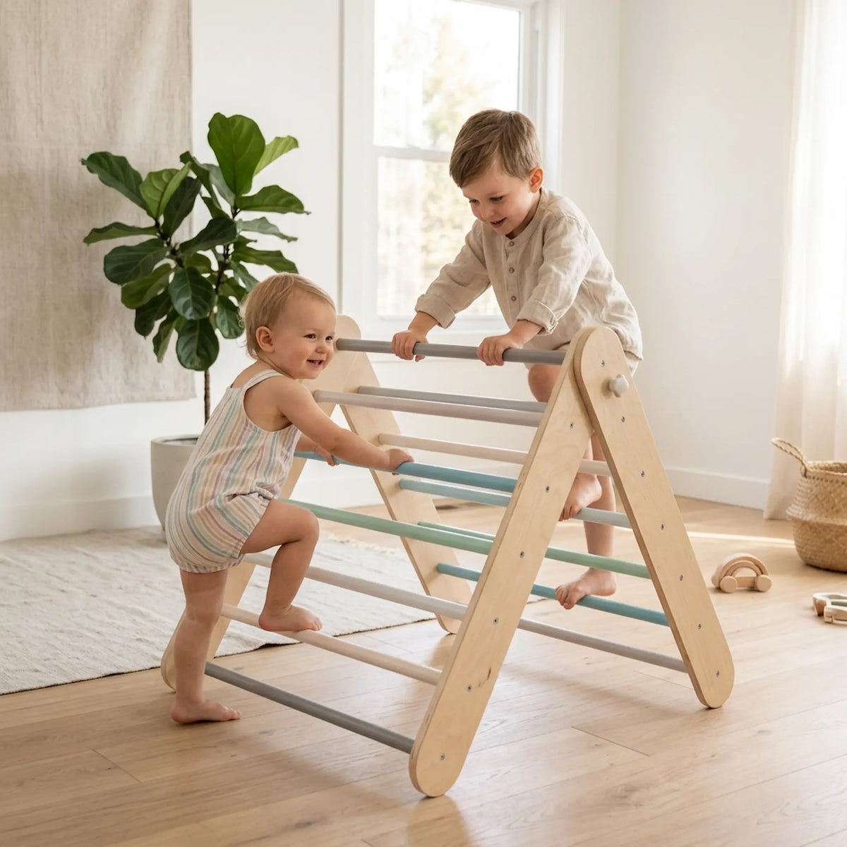 Two toddlers play on a natural wood A-frame climbing ladder with gray and teal bars in a bright, modern room with wood floors and a potted plant.