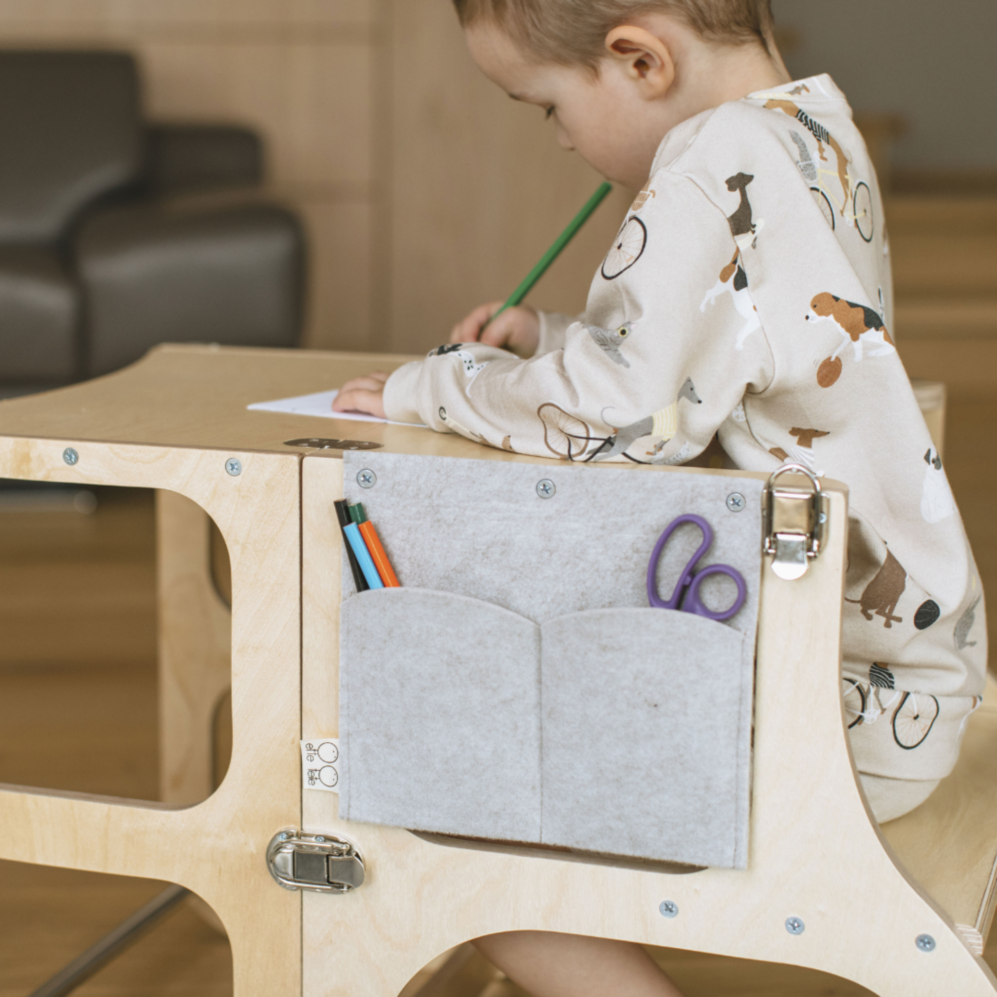 Child drawing at a wooden Montessori desk with a felt pencil case organizer attached