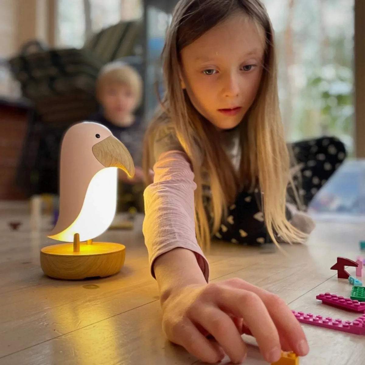 Child playing with toys near a flamingo-shaped night light on a wooden floor.