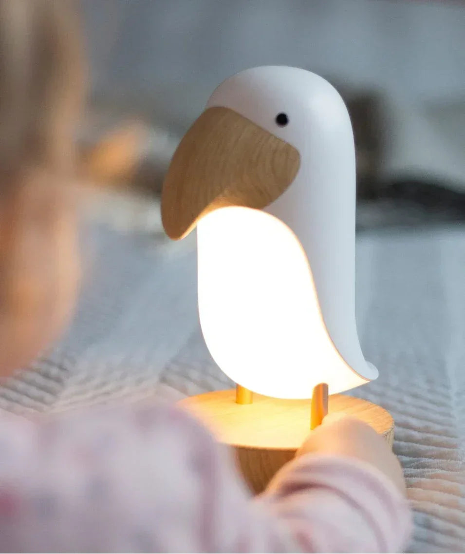Child using bird-shaped Montessori night light with wooden base on cozy bed