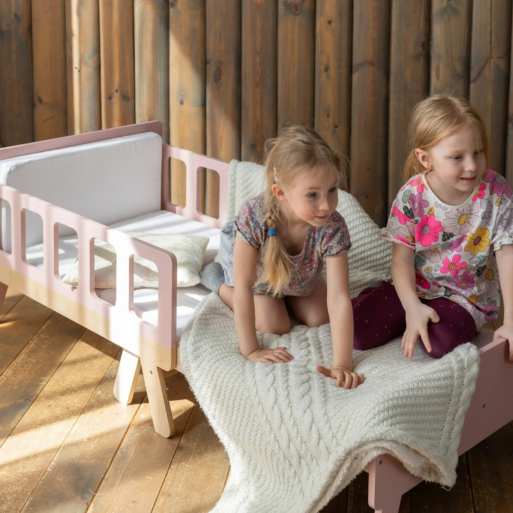 Two children on a Montessori-inspired wooden toddler bed with a white knit blanket.