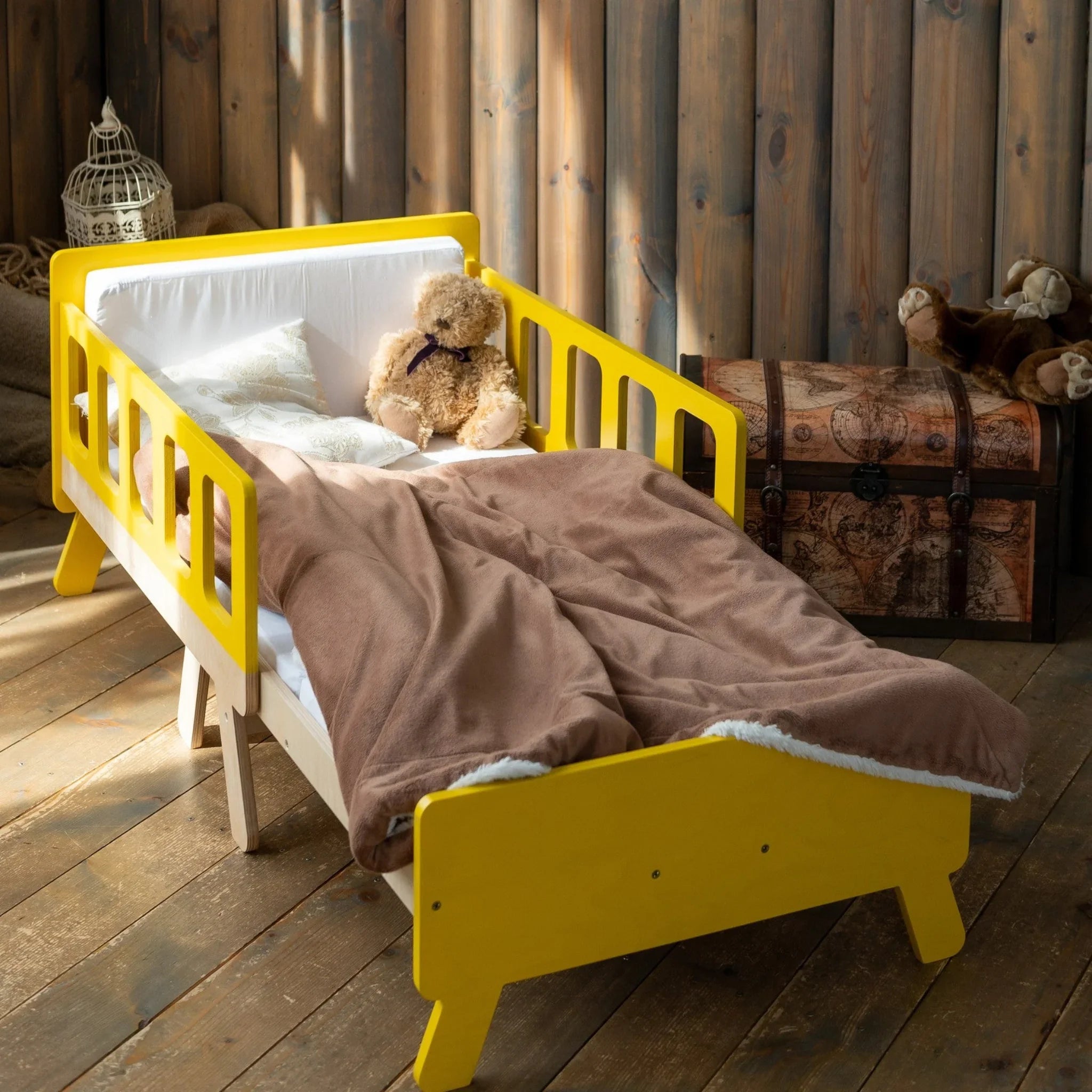 Montessori-inspired yellow wooden kids bed with safety rails and teddy bear in cozy room