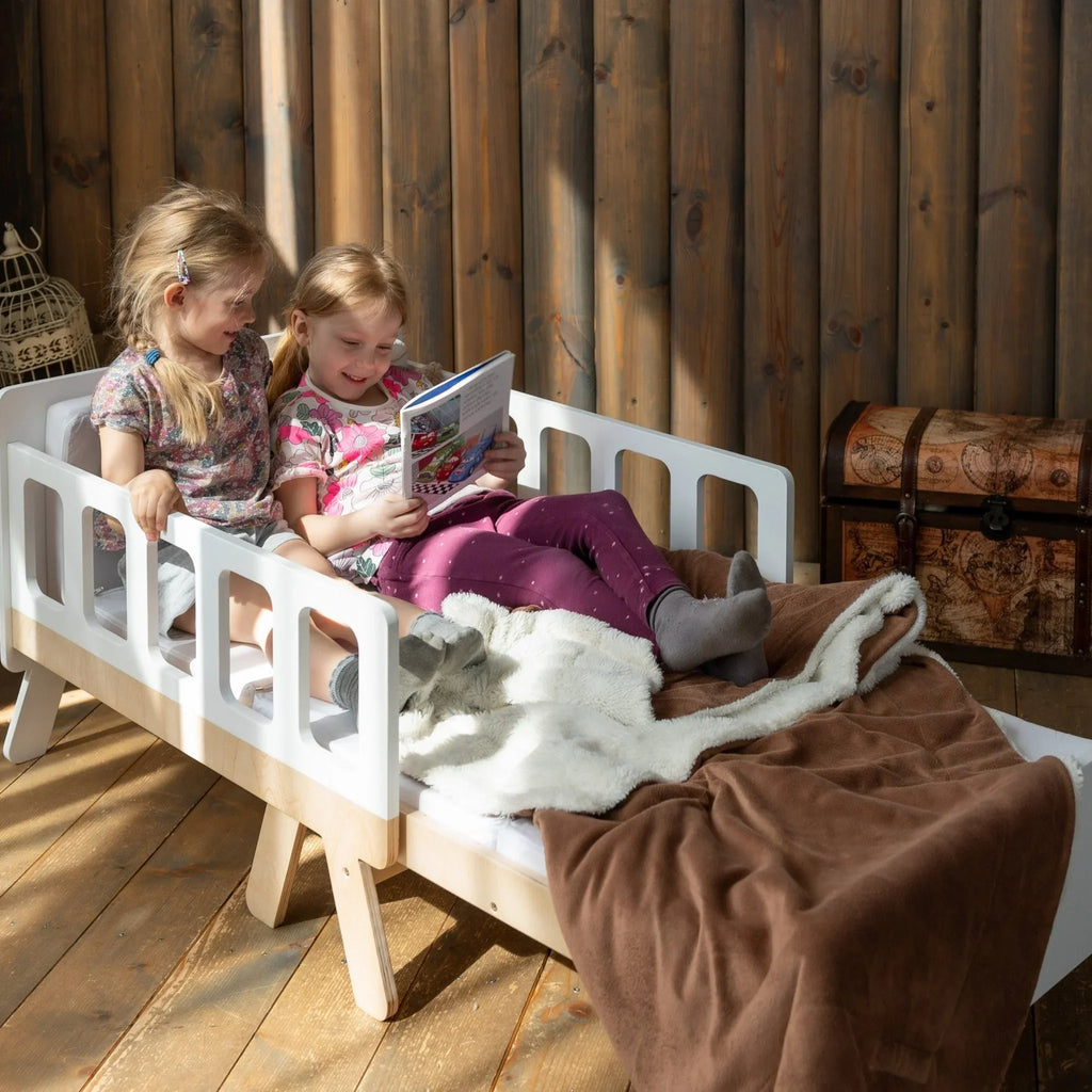 Two children reading on a Montessori-inspired wooden kids bed with cozy blankets.