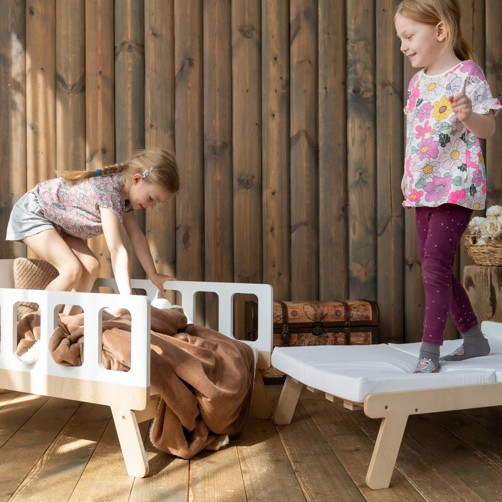 Two girls playing on Montessori-inspired wooden kids beds in a cozy room with wooden walls.