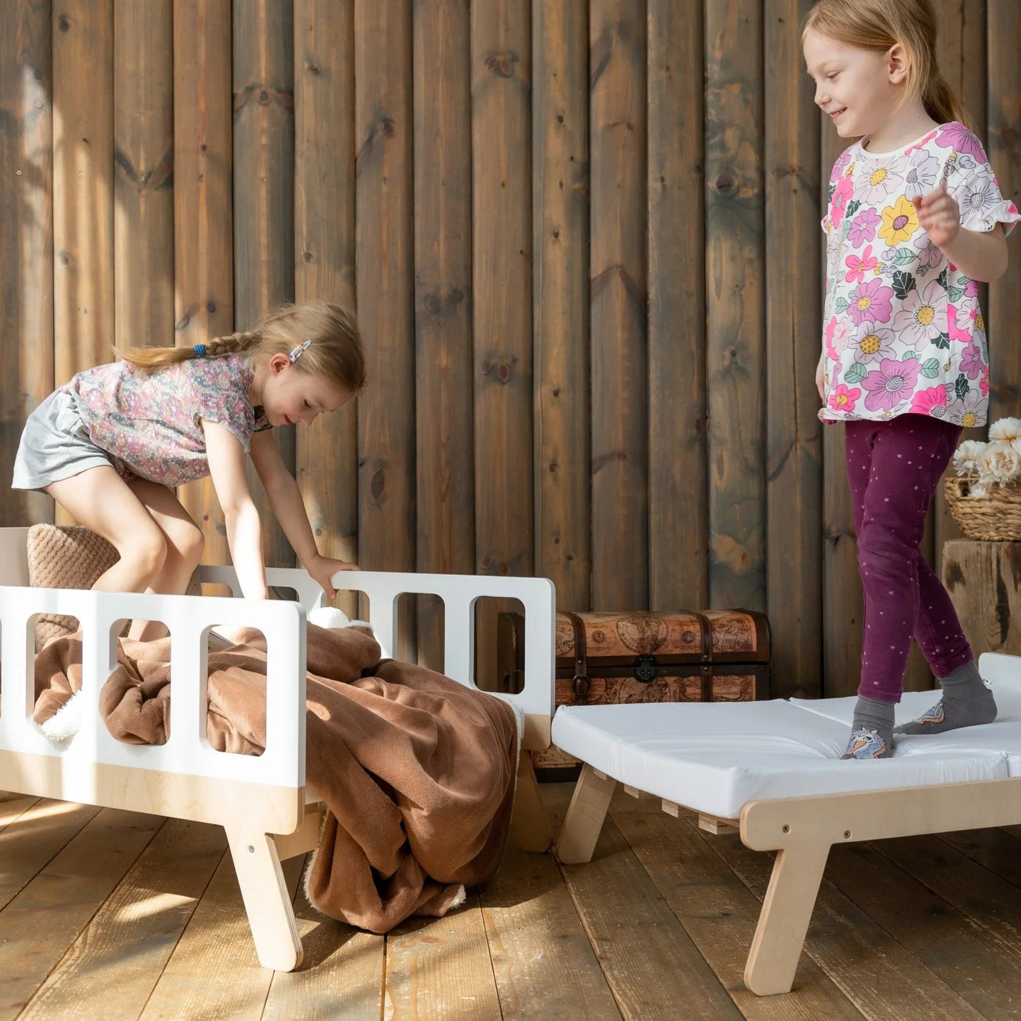 Two girls playing on Montessori-inspired wooden kids beds in a cozy room with wooden walls.