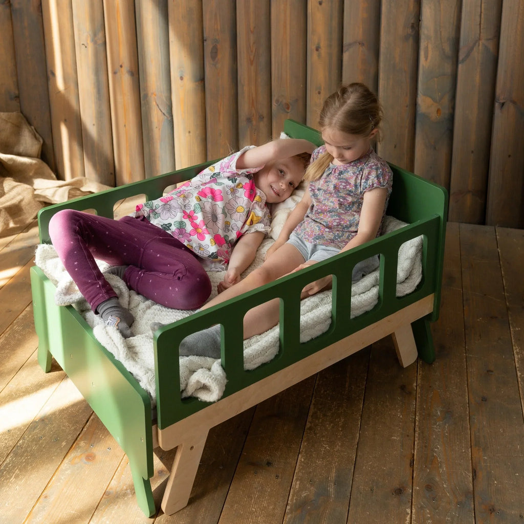 Two young children in a green Montessori-inspired wooden toddler bed with side rails.