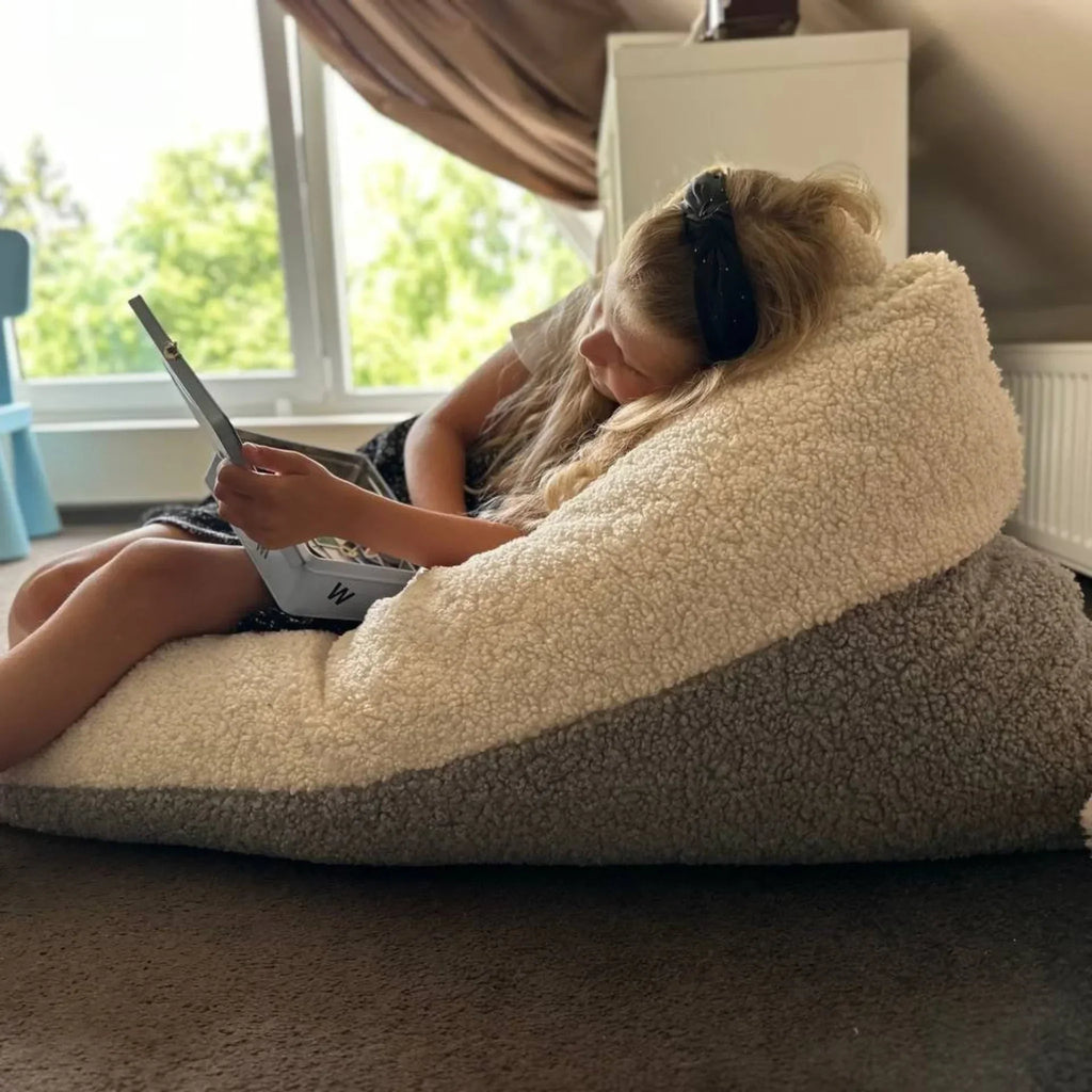 Child reading on a cozy two-tone sherpa bean bag chair in a bright attic room