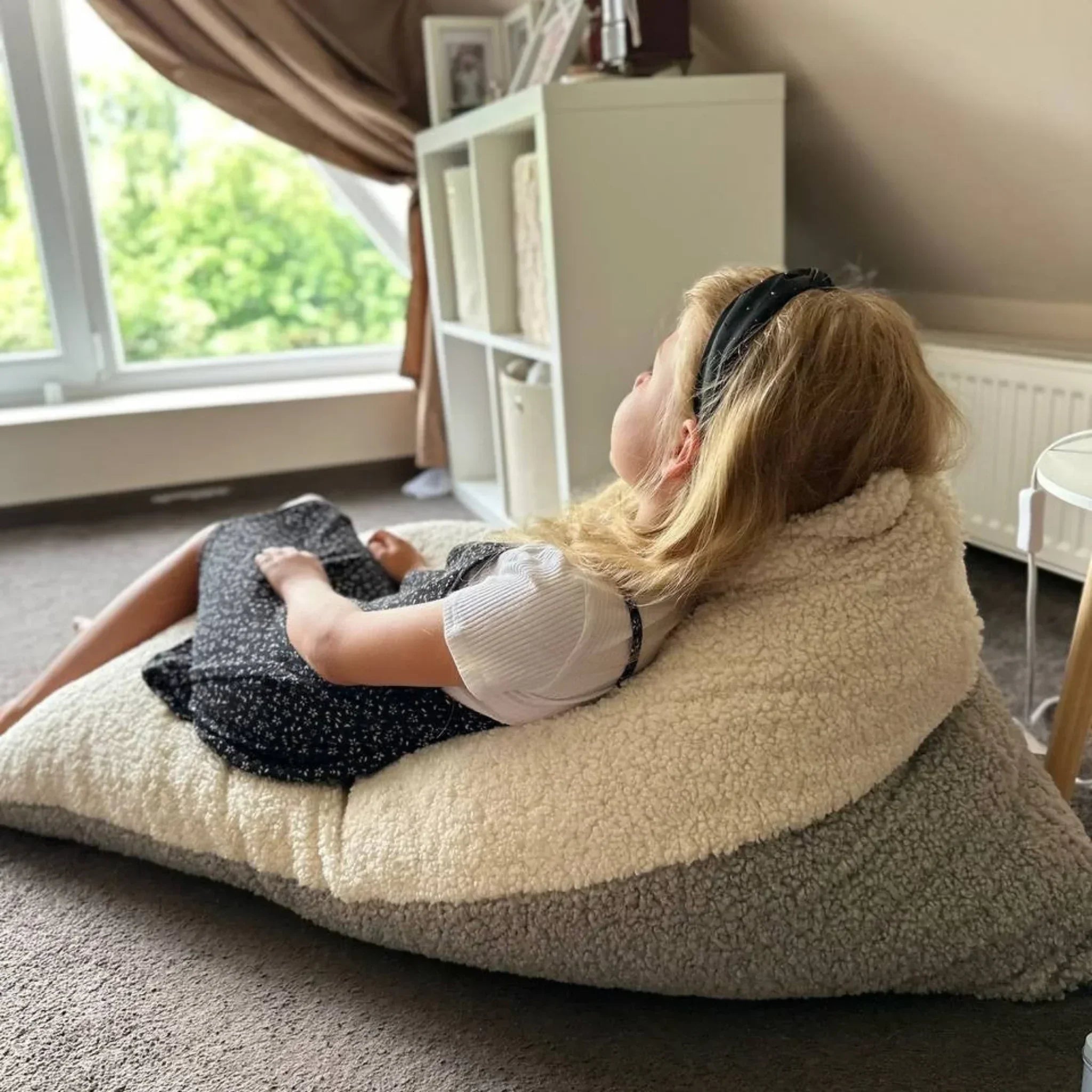 Child relaxing on plush Montessori-inspired bean bag chair in cozy room with natural light.