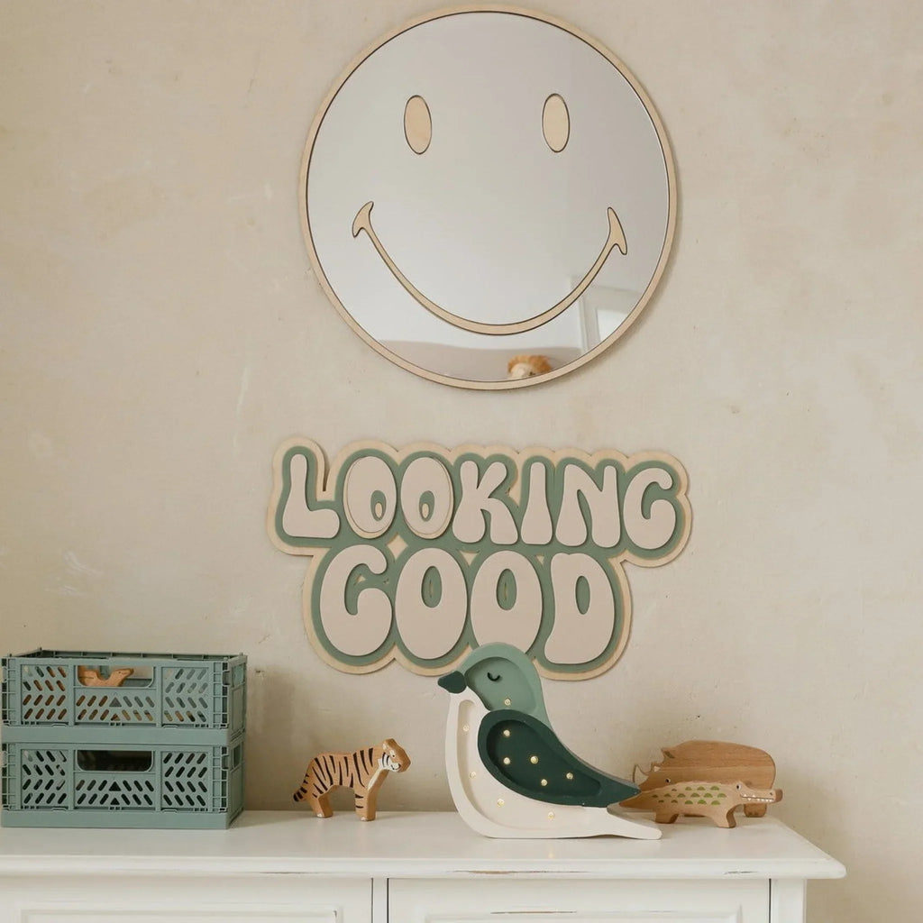 Kids room with smiley face mirror, 'Looking Good' wall sign, and wooden animal toys on dresser.