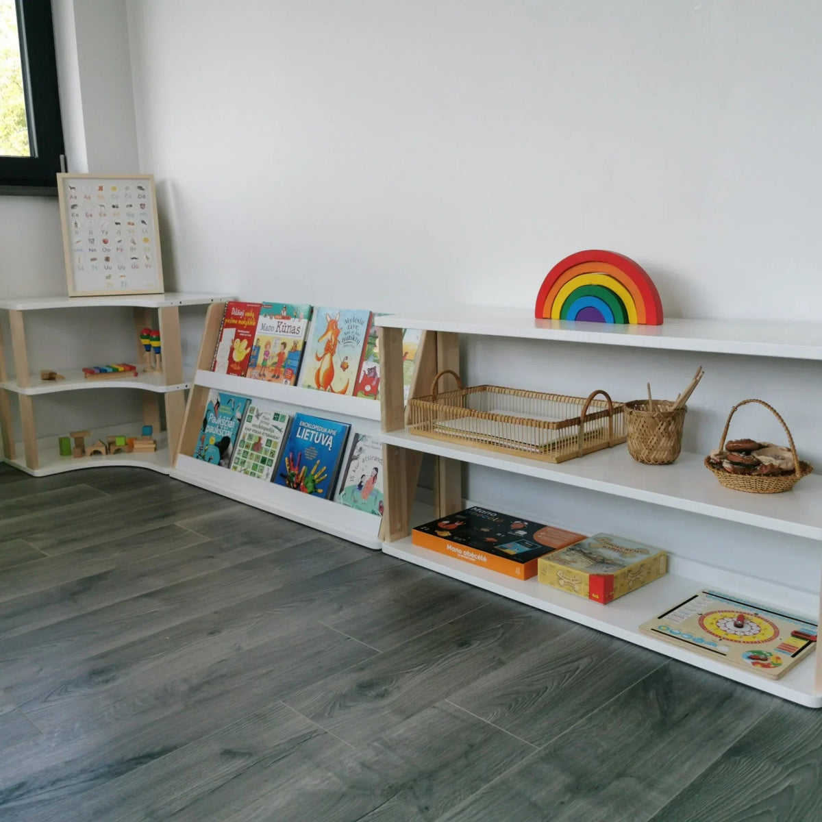 Children's playroom with shelves displaying books, toys, and a rainbow decoration.