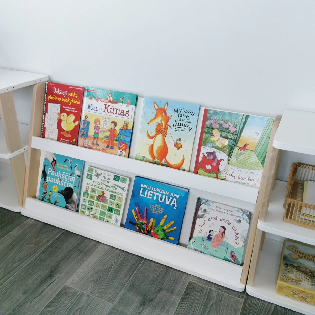 Children's books on a white bookshelf against a light gray wall.