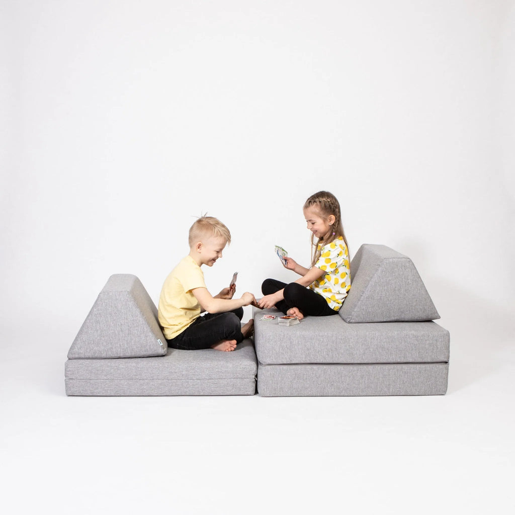 Two children sitting on a gray wedge-shaped sofa against a white background