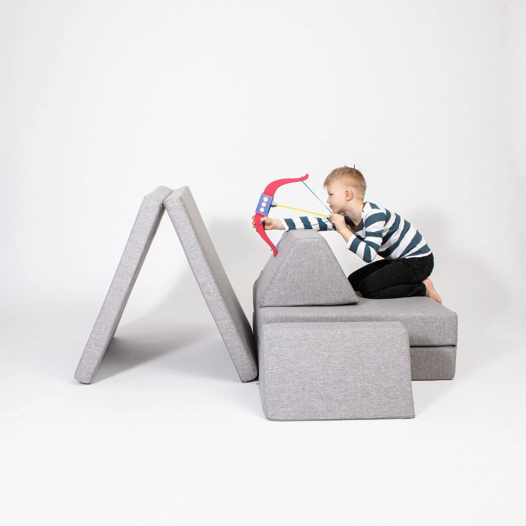 Child playing with a toy bow and arrow on a gray modular furniture piece against a white background