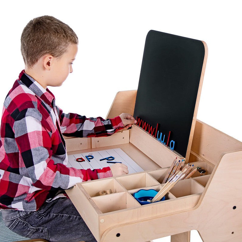 Child at Montessori-inspired wooden art desk with chalkboard and storage compartments.