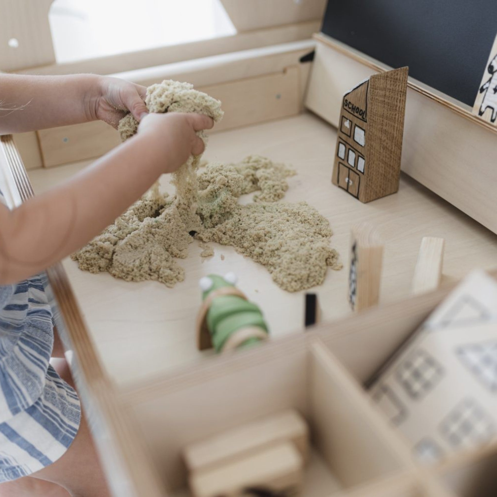 Child playing with sensory sand and wooden Montessori toys on a light wooden activity table