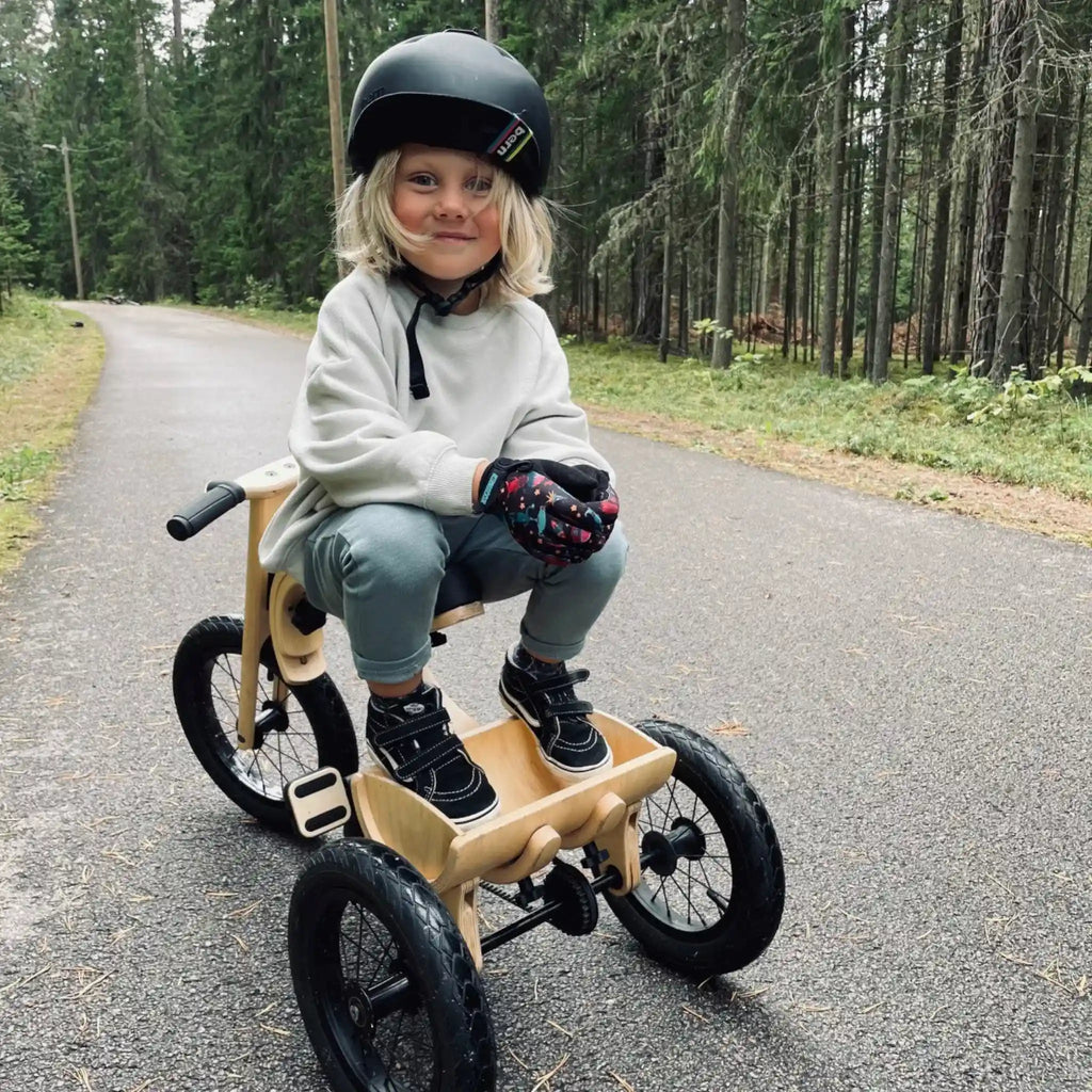 Child riding a wooden bike on a paved road with a forest in the background