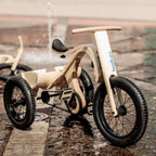 Children's wooden balance bike with training wheels on a wet pavement.